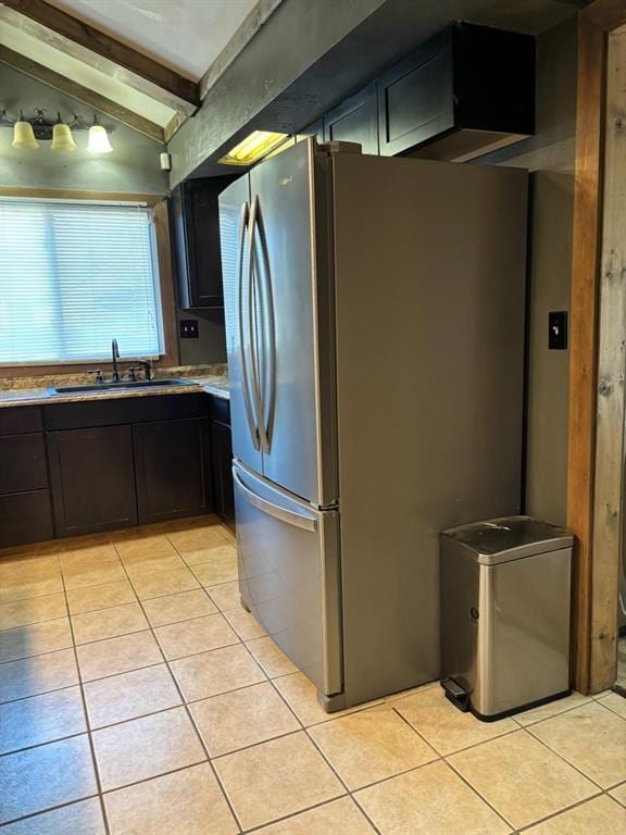 kitchen featuring light tile patterned floors, lofted ceiling with beams, stainless steel fridge, and sink