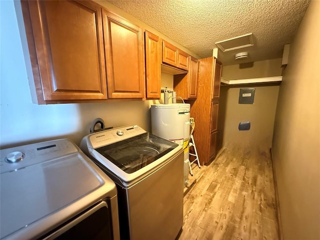 clothes washing area with water heater, a textured ceiling, washing machine and dryer, cabinets, and light hardwood / wood-style flooring