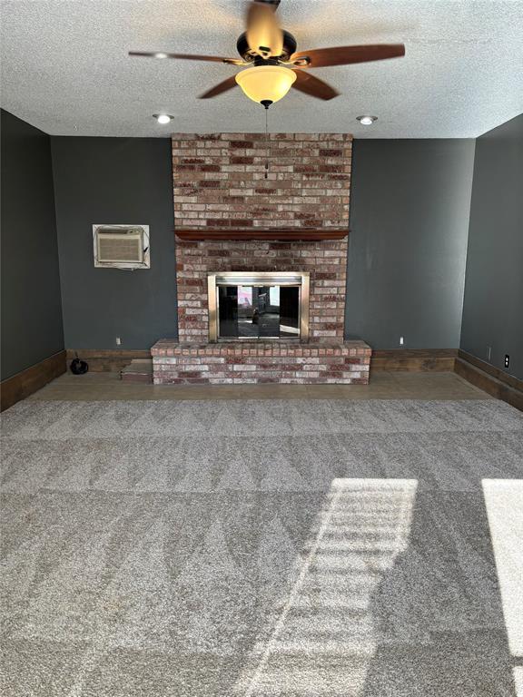 unfurnished living room with ceiling fan, a fireplace, and a textured ceiling