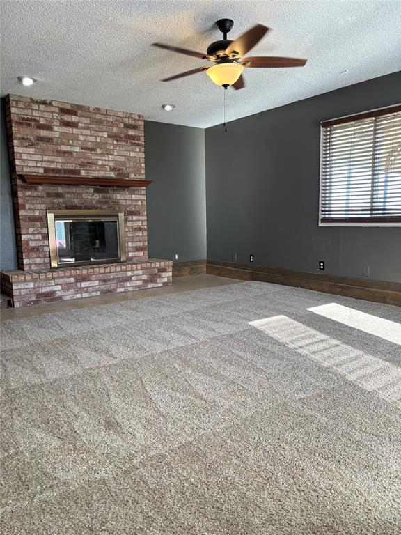 unfurnished living room with a textured ceiling, ceiling fan, carpet flooring, and a brick fireplace