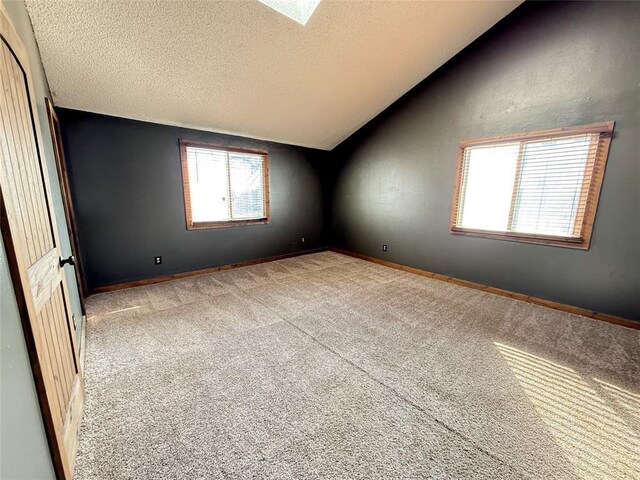 carpeted empty room with a textured ceiling, a healthy amount of sunlight, and vaulted ceiling