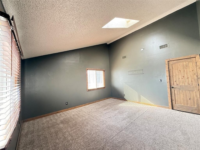 carpeted empty room with a textured ceiling, lofted ceiling with skylight, and a barn door