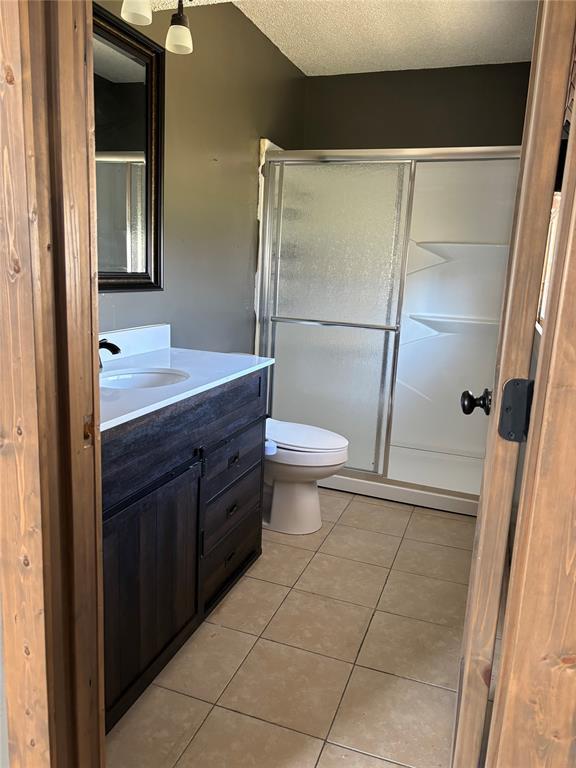 bathroom with a textured ceiling, tile patterned flooring, vanity, toilet, and a shower with shower door