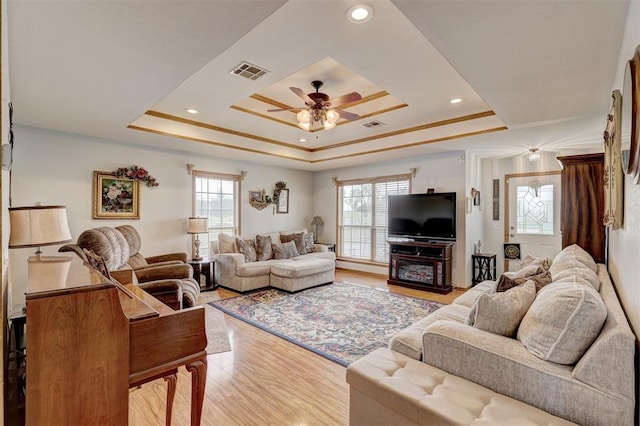 living room with a raised ceiling, a wealth of natural light, light hardwood / wood-style flooring, and ceiling fan