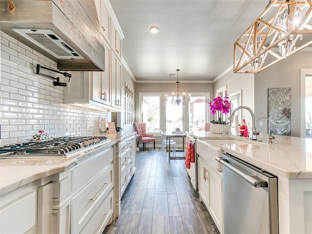 kitchen featuring a center island with sink, appliances with stainless steel finishes, decorative light fixtures, light stone counters, and white cabinetry