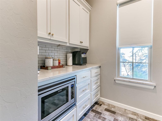 bar with backsplash, light stone countertops, stainless steel microwave, and white cabinets