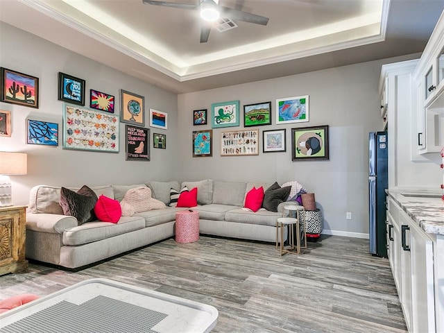 living room featuring light hardwood / wood-style flooring, a raised ceiling, and ceiling fan