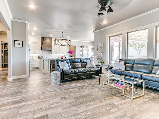 living room with crown molding, visible vents, baseboards, a ceiling fan, and light wood finished floors