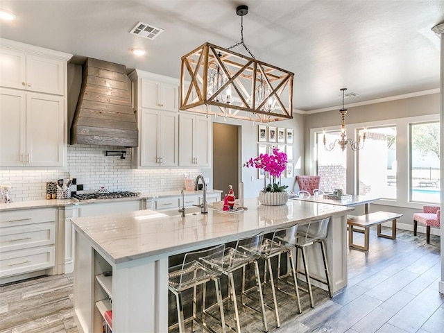 kitchen featuring visible vents, premium range hood, white cabinets, tasteful backsplash, and a sink