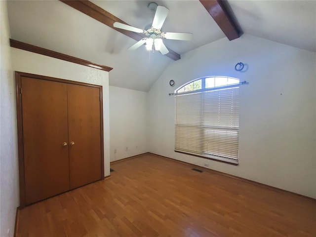 unfurnished bedroom with hardwood / wood-style flooring, ceiling fan, lofted ceiling with beams, and a closet