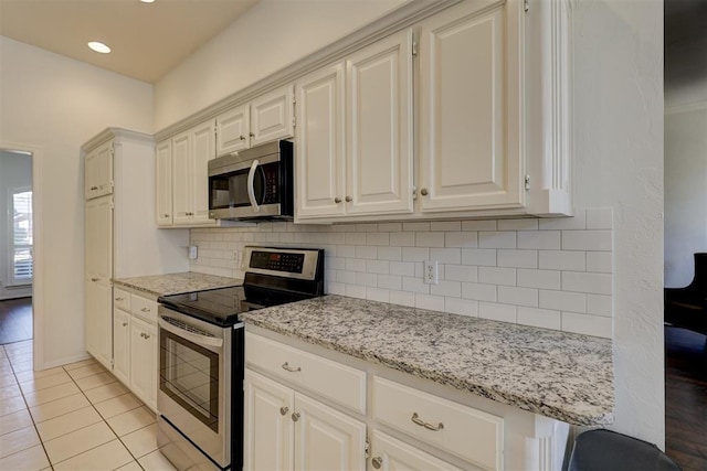 kitchen with decorative backsplash, light stone countertops, stainless steel appliances, white cabinetry, and light tile patterned flooring