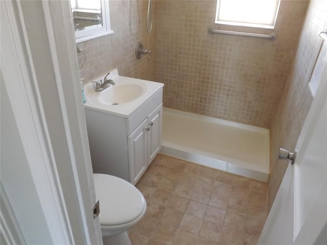 bathroom with tile patterned floors, a tile shower, vanity, tile walls, and toilet