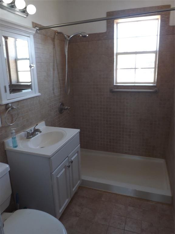 bathroom featuring decorative backsplash, a tile shower, vanity, tile patterned flooring, and toilet