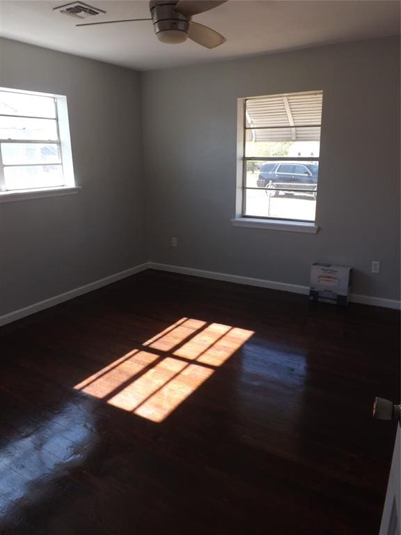 spare room featuring dark wood-type flooring, ceiling fan, and a healthy amount of sunlight