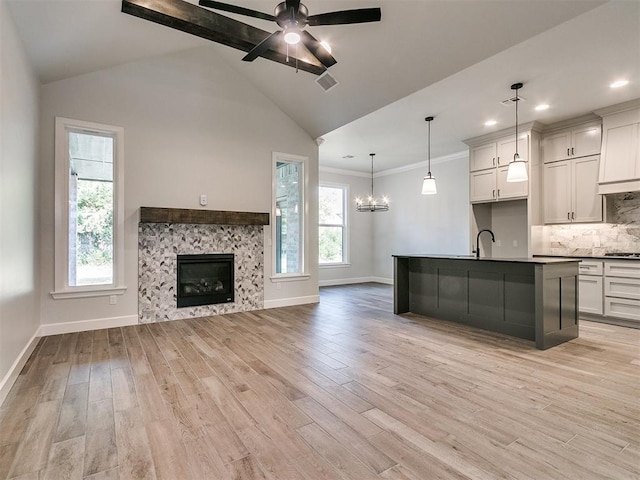 kitchen featuring a fireplace, light wood-type flooring, a center island with sink, and hanging light fixtures