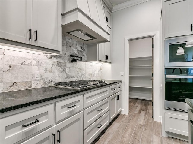 kitchen featuring white cabinets, light wood-type flooring, custom range hood, and dark stone counters