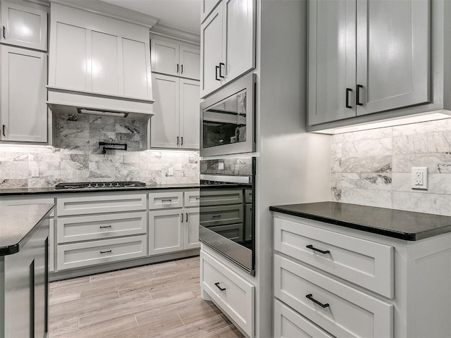 kitchen featuring backsplash, stainless steel appliances, light hardwood / wood-style floors, and range hood