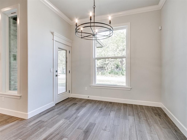 unfurnished dining area featuring plenty of natural light, light wood-type flooring, ornamental molding, and a chandelier