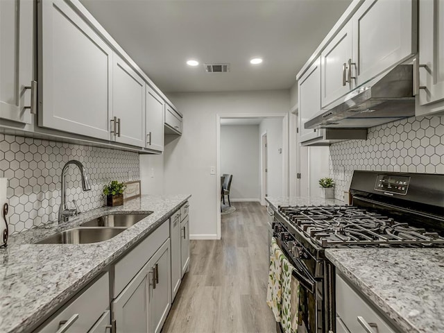 kitchen with backsplash, sink, light wood-type flooring, and black gas range oven