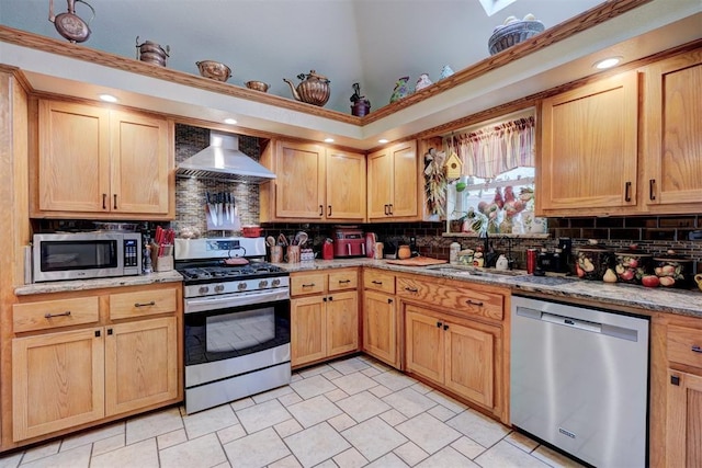 kitchen featuring sink, light stone counters, tasteful backsplash, appliances with stainless steel finishes, and wall chimney range hood