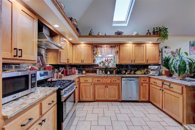 kitchen with wall chimney range hood, sink, appliances with stainless steel finishes, vaulted ceiling with skylight, and light stone countertops