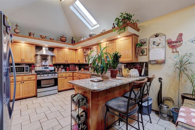 kitchen featuring wall chimney exhaust hood, light stone counters, a skylight, appliances with stainless steel finishes, and kitchen peninsula