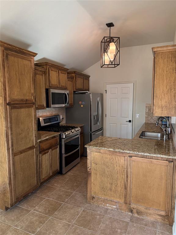 kitchen featuring backsplash, stainless steel appliances, sink, hanging light fixtures, and lofted ceiling