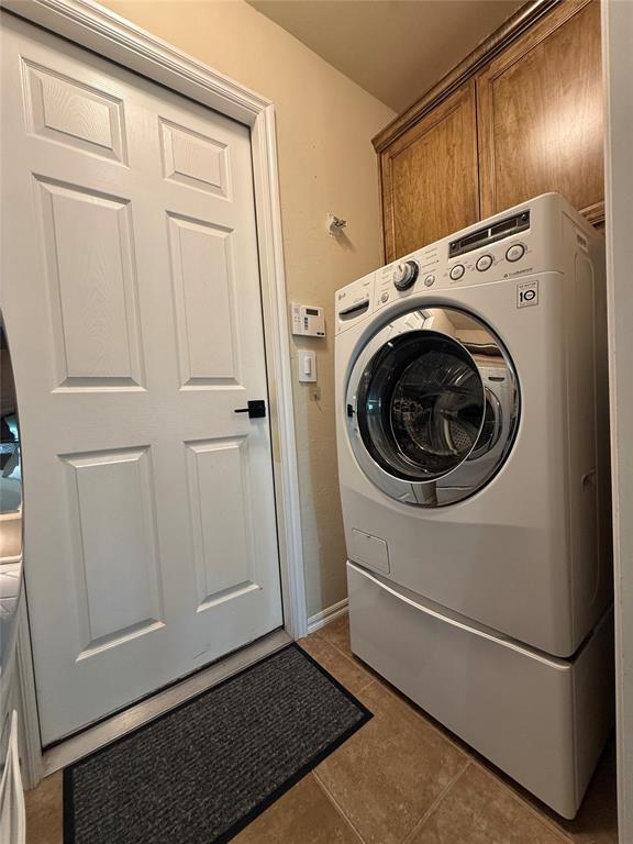 clothes washing area featuring cabinets, washer / dryer, and dark tile patterned flooring