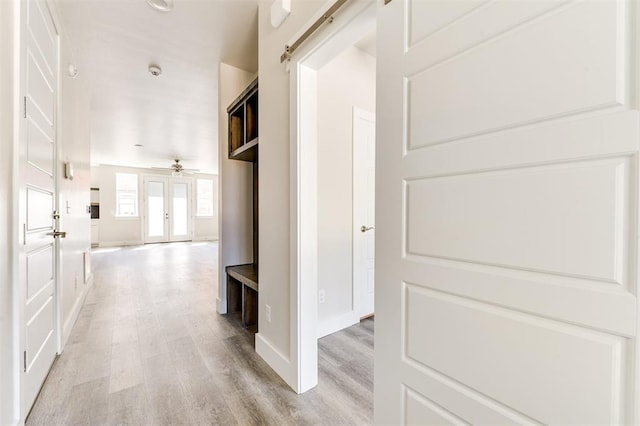 corridor featuring french doors, a barn door, and light hardwood / wood-style flooring