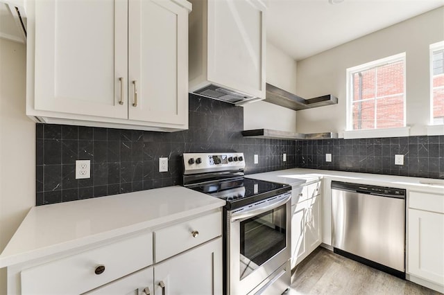 kitchen featuring premium range hood, white cabinets, decorative backsplash, light wood-type flooring, and stainless steel appliances