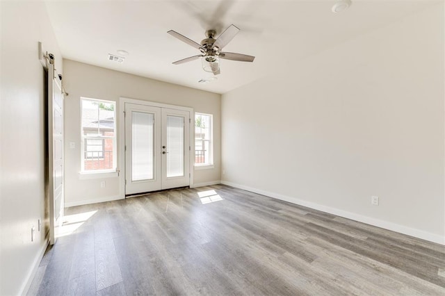 empty room with french doors, a barn door, light hardwood / wood-style flooring, and ceiling fan