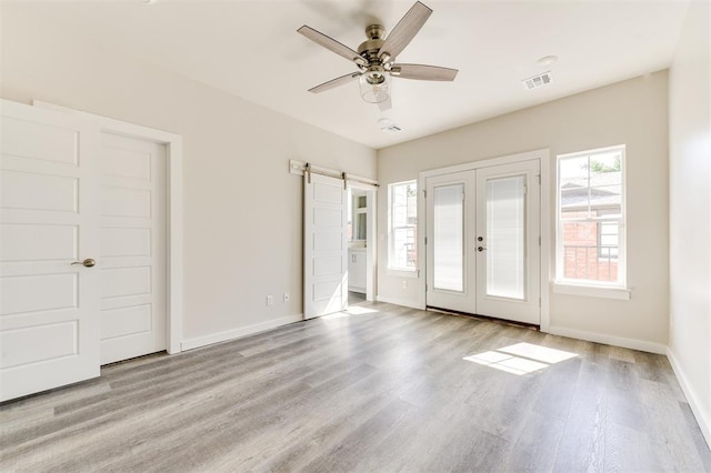 unfurnished bedroom with a barn door, ceiling fan, light hardwood / wood-style flooring, and french doors