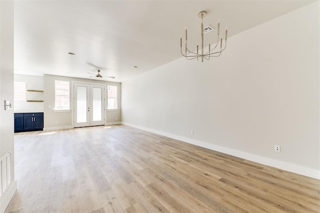 unfurnished living room with ceiling fan with notable chandelier and light hardwood / wood-style flooring