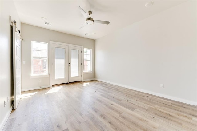 unfurnished room with a barn door, ceiling fan, light hardwood / wood-style flooring, and french doors