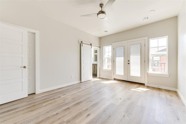 unfurnished bedroom with ceiling fan, a barn door, french doors, and light hardwood / wood-style flooring