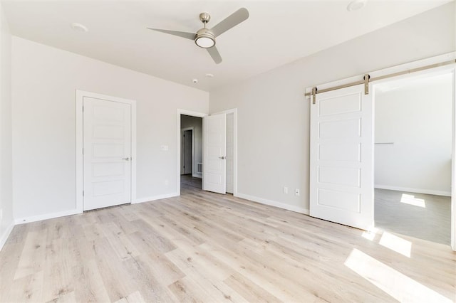 unfurnished bedroom featuring light wood-type flooring, a barn door, and ceiling fan