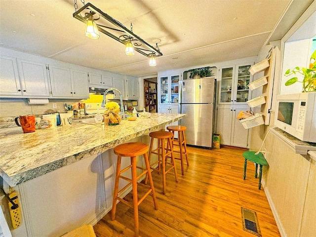 kitchen featuring stainless steel fridge, light hardwood / wood-style flooring, white cabinetry, and a breakfast bar area