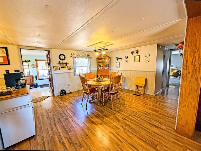 dining room featuring hardwood / wood-style floors, wood walls, and a textured ceiling