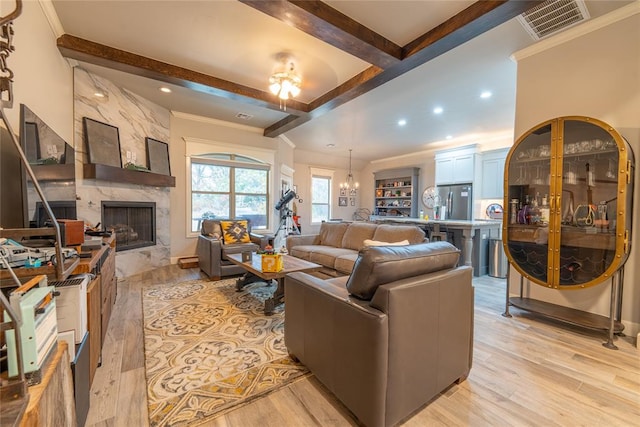 living room featuring ornamental molding, a fireplace, beamed ceiling, a notable chandelier, and light hardwood / wood-style floors