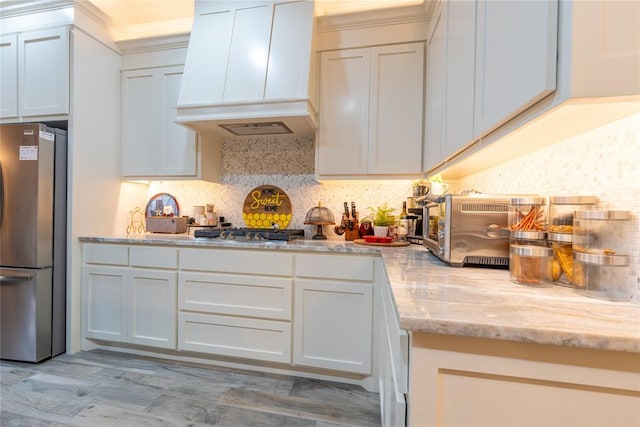 kitchen featuring light stone counters, white cabinets, stainless steel appliances, and custom range hood