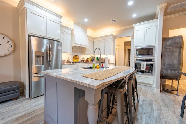 kitchen with appliances with stainless steel finishes, light stone counters, light hardwood / wood-style floors, white cabinetry, and an island with sink