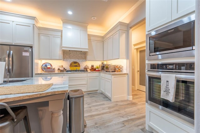 kitchen featuring light stone countertops, appliances with stainless steel finishes, light wood-type flooring, decorative backsplash, and white cabinetry