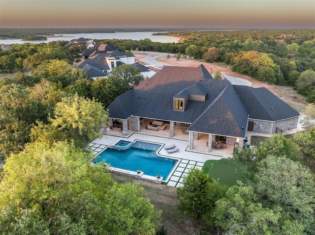 pool at dusk featuring a water view and a patio area