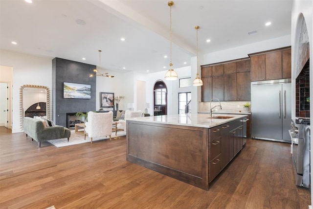 kitchen with dark brown cabinetry, sink, dark wood-type flooring, stainless steel appliances, and a kitchen island with sink