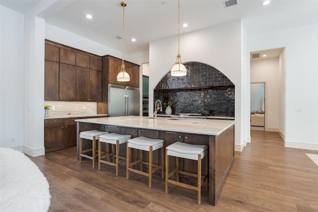 kitchen with hanging light fixtures, tasteful backsplash, stainless steel built in fridge, and wood-type flooring