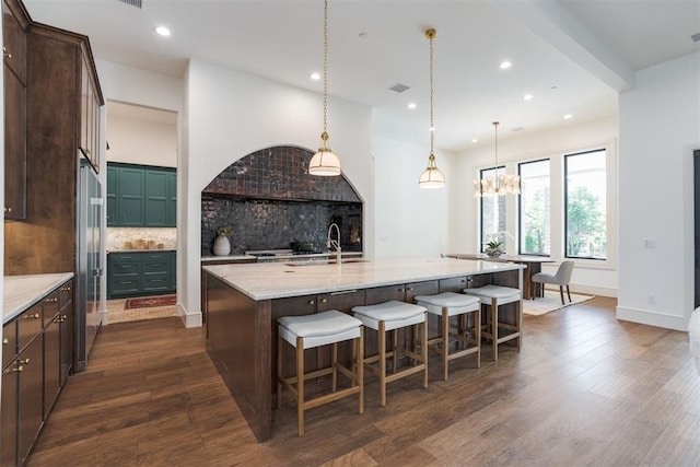 kitchen with dark hardwood / wood-style floors, decorative backsplash, light stone countertops, and a large island with sink