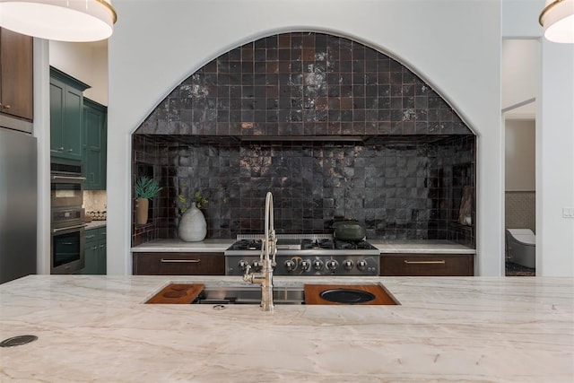 interior space featuring green cabinets, sink, appliances with stainless steel finishes, tasteful backsplash, and light stone counters