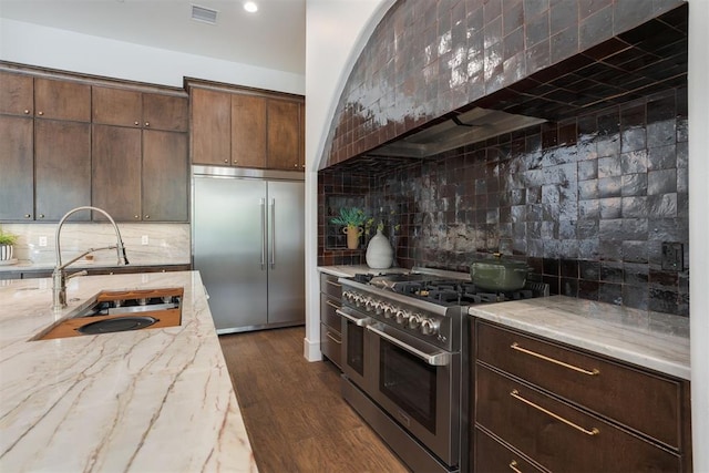 kitchen featuring decorative backsplash, dark brown cabinets, premium appliances, dark wood-type flooring, and sink