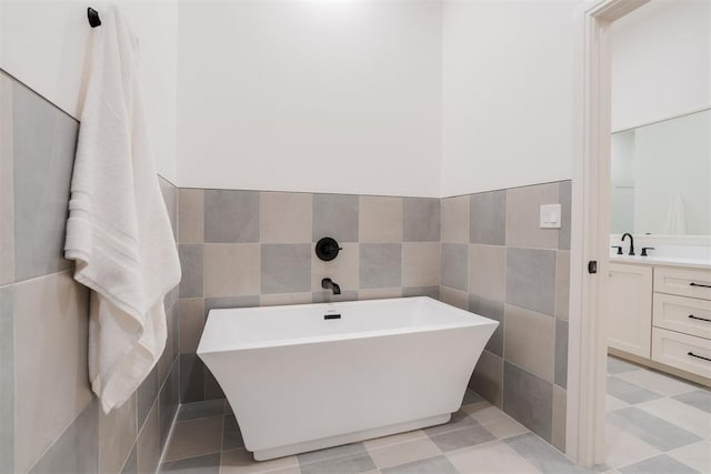 bathroom with a bath, vanity, and tile walls