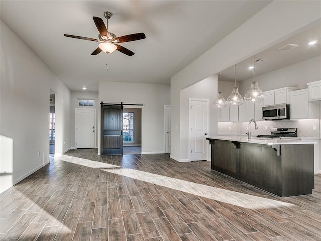 kitchen featuring hardwood / wood-style floors, white cabinets, a barn door, an island with sink, and stainless steel appliances